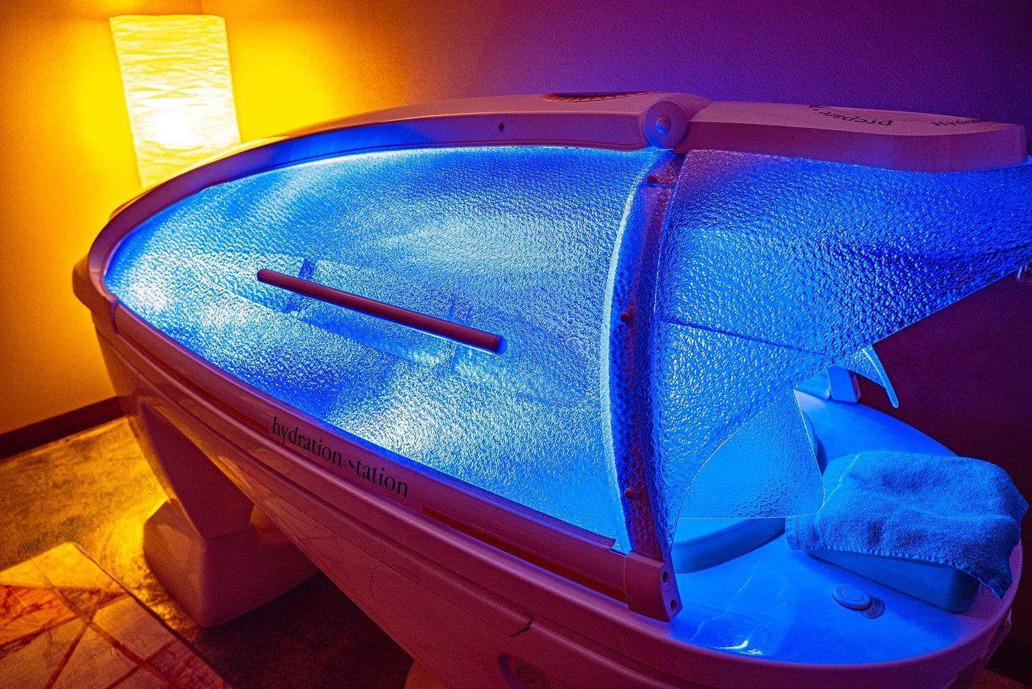 An illuminated spa hydration station bathes in calming blue light, set against a warm, orange-lit room. The scene evokes relaxation and tranquility.